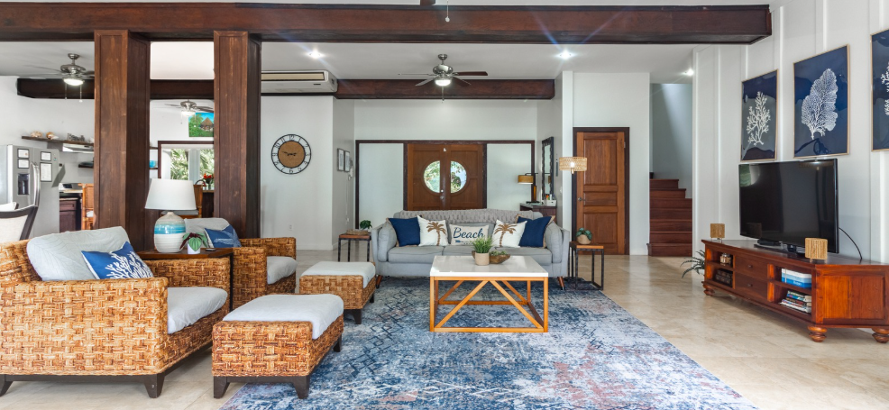 Living room with blue rug, wicker furniture, and wooden beams.