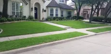 A house with a lush green lawn and a sidewalk in front of it.