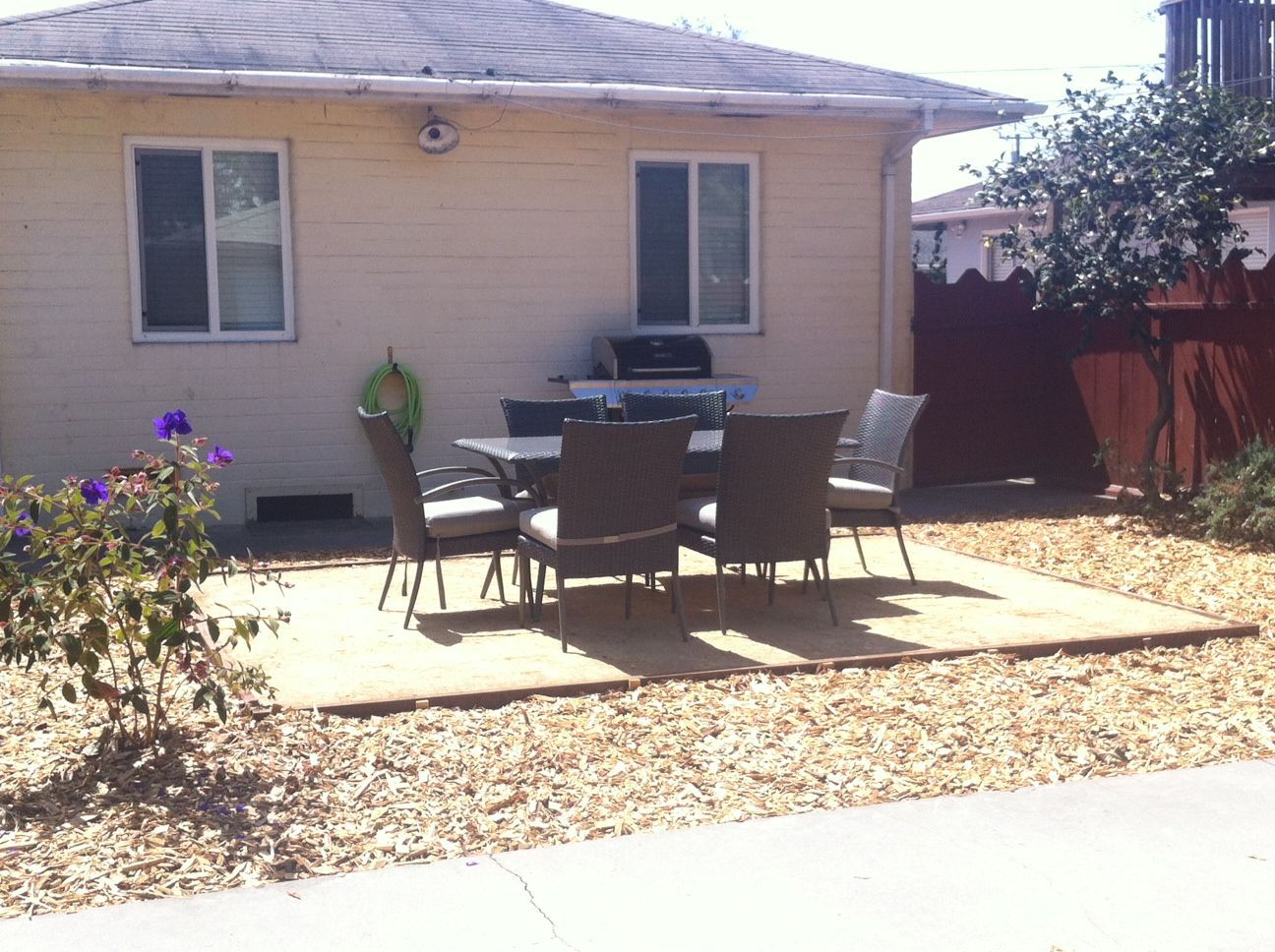 Backyard patio with outdoor dining table, chairs, and a barbecue grill beside a beige house