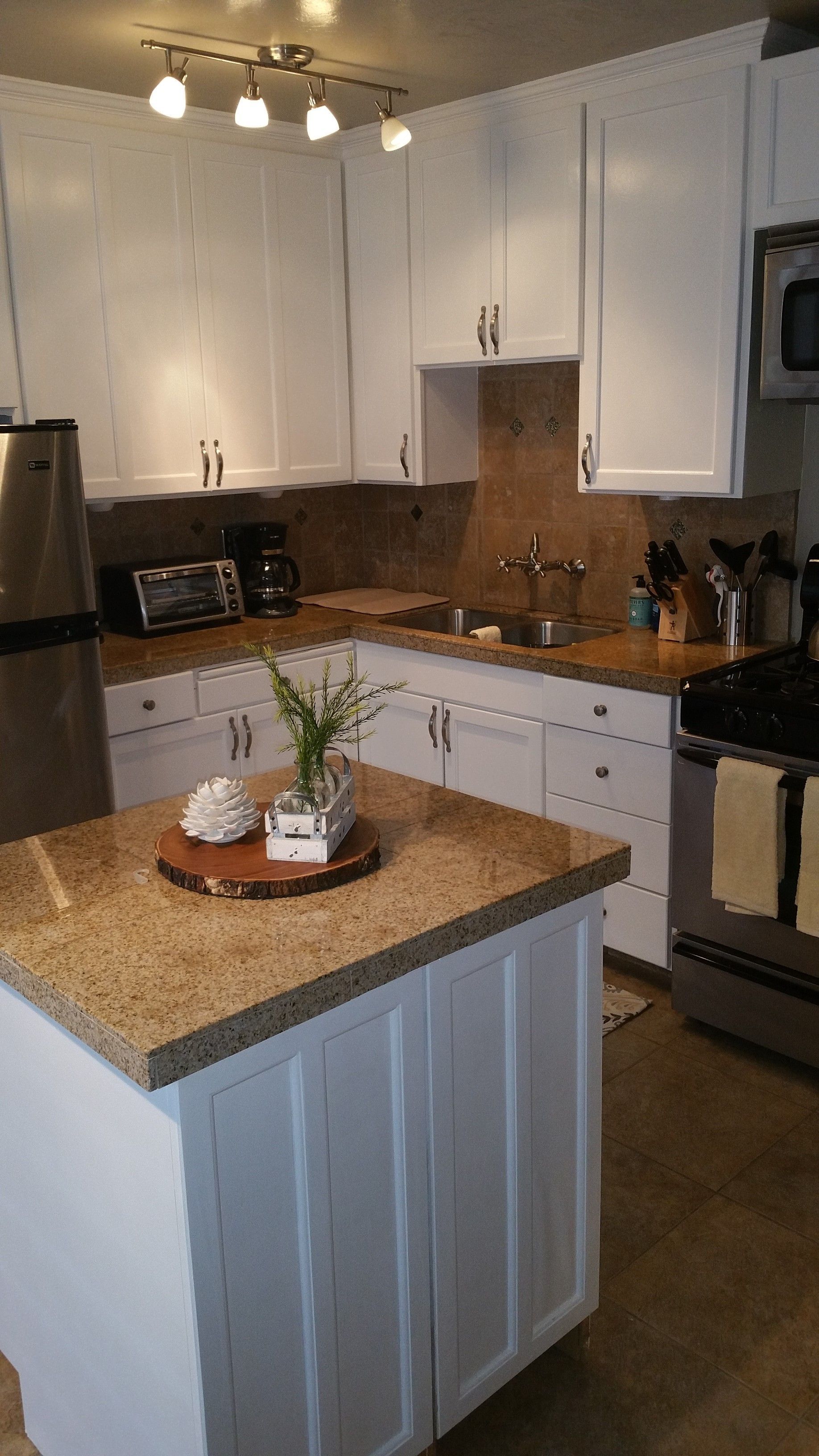 Modern kitchen with white cabinets, tan countertops, center island, and stainless steel stove and refrigerator.