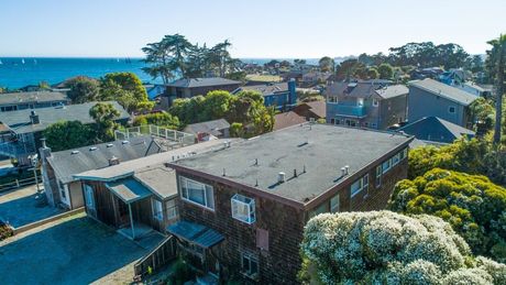 Aerial view of a coastal neighborhood with a brick building, trees, and ocean in the background