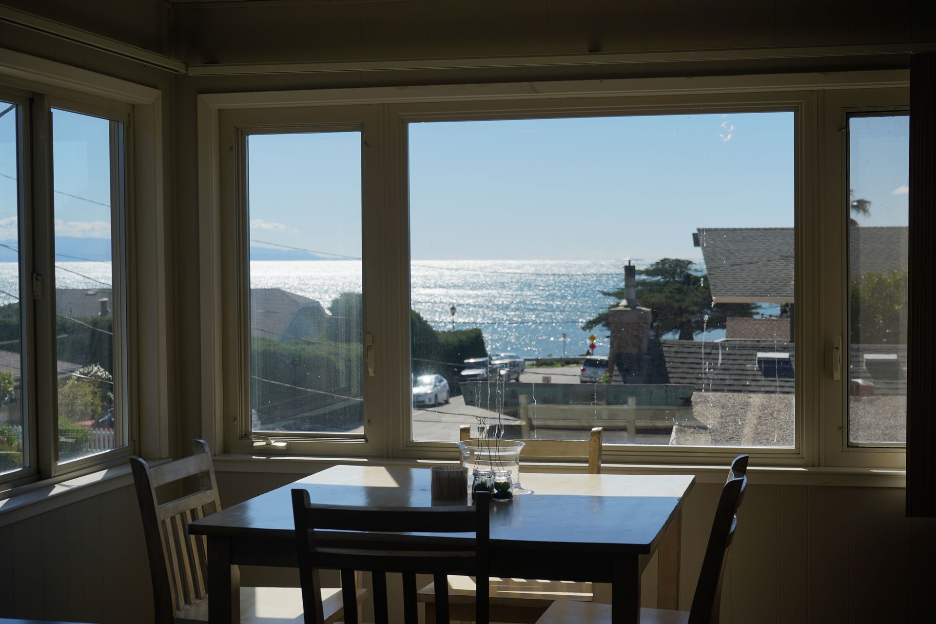 Dining table by large windows overlooking a sunlit ocean view