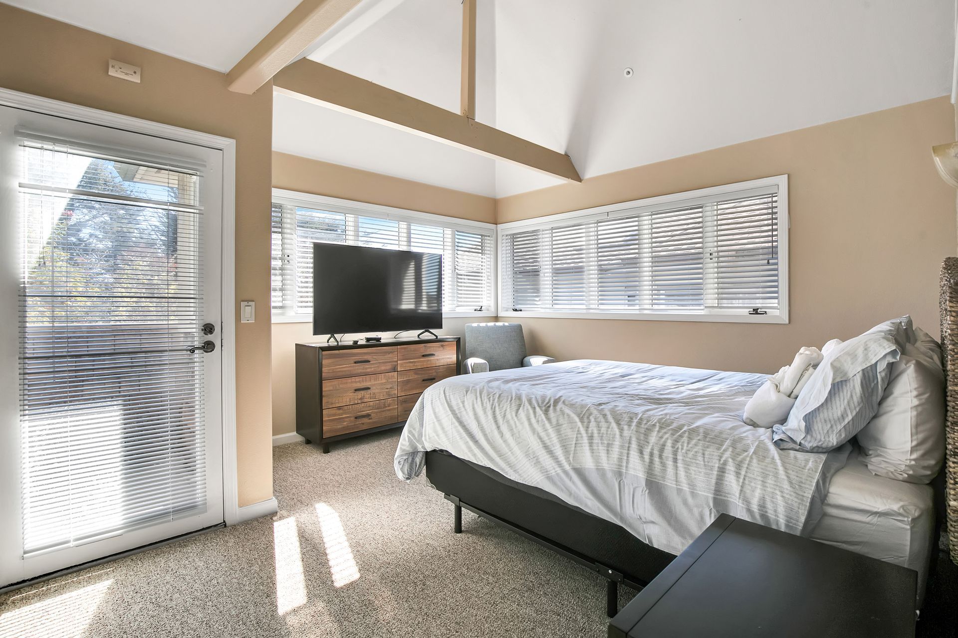Bright bedroom with a bed, dresser, TV, and large windows letting in sunlight