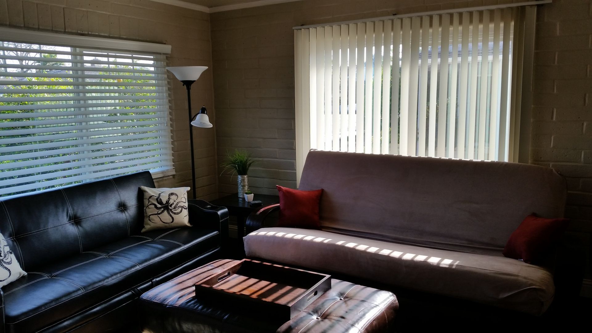 Living room with black leather sofa, chaise lounge, window blinds, and warm-toned decor