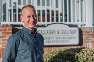 A man is standing in front of a building with a sign that says callahan & calloway property management professionals.