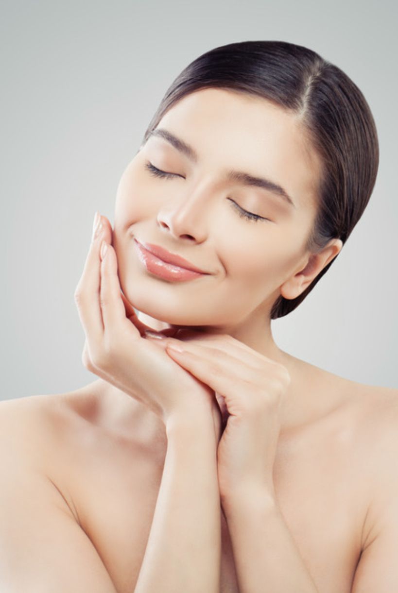 Une femme touche son visage avec ses mains et sourit.