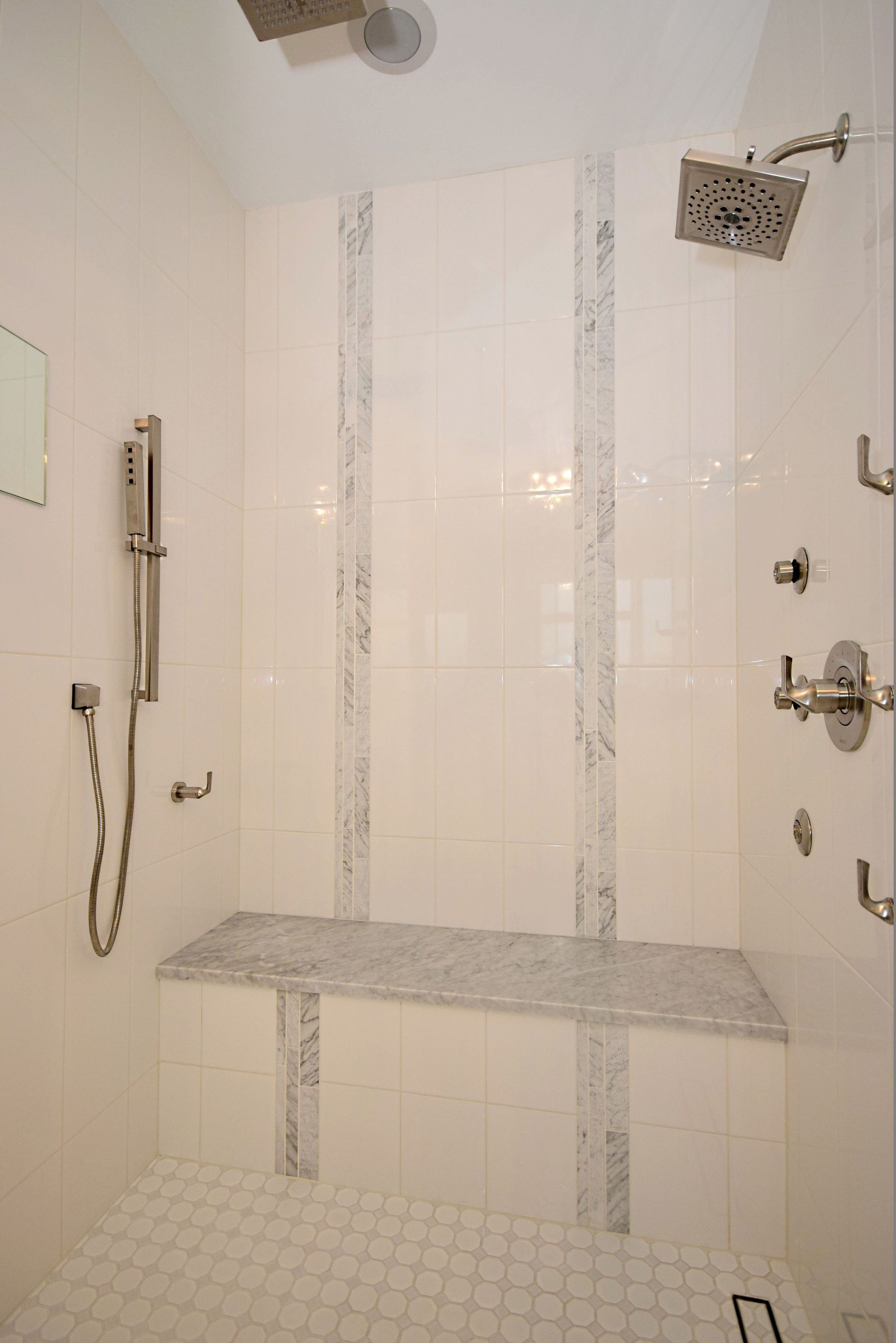 A bathroom with a walk in shower with a bench and a shower head.