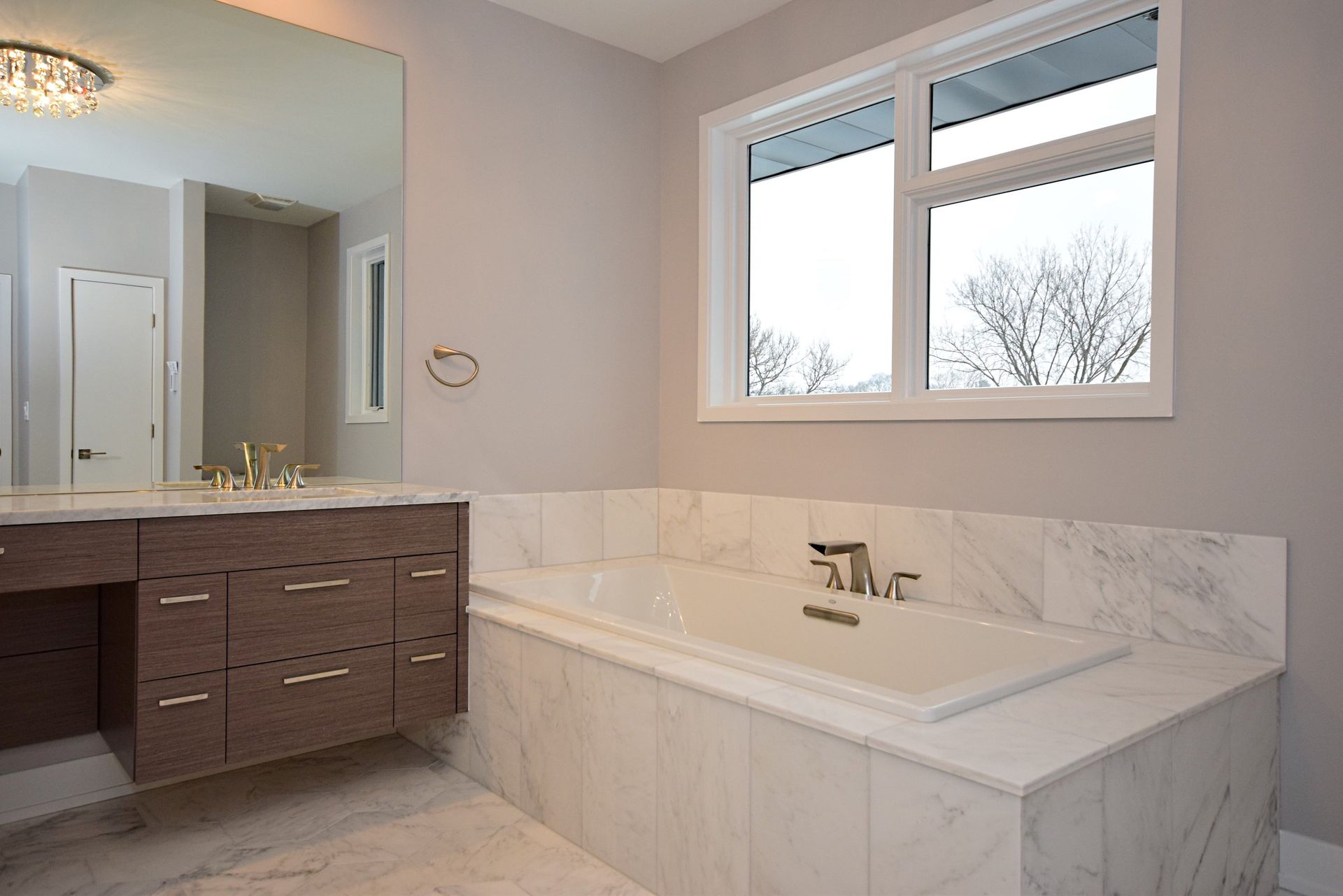 A bathroom with a tub , sink , mirror and window.
