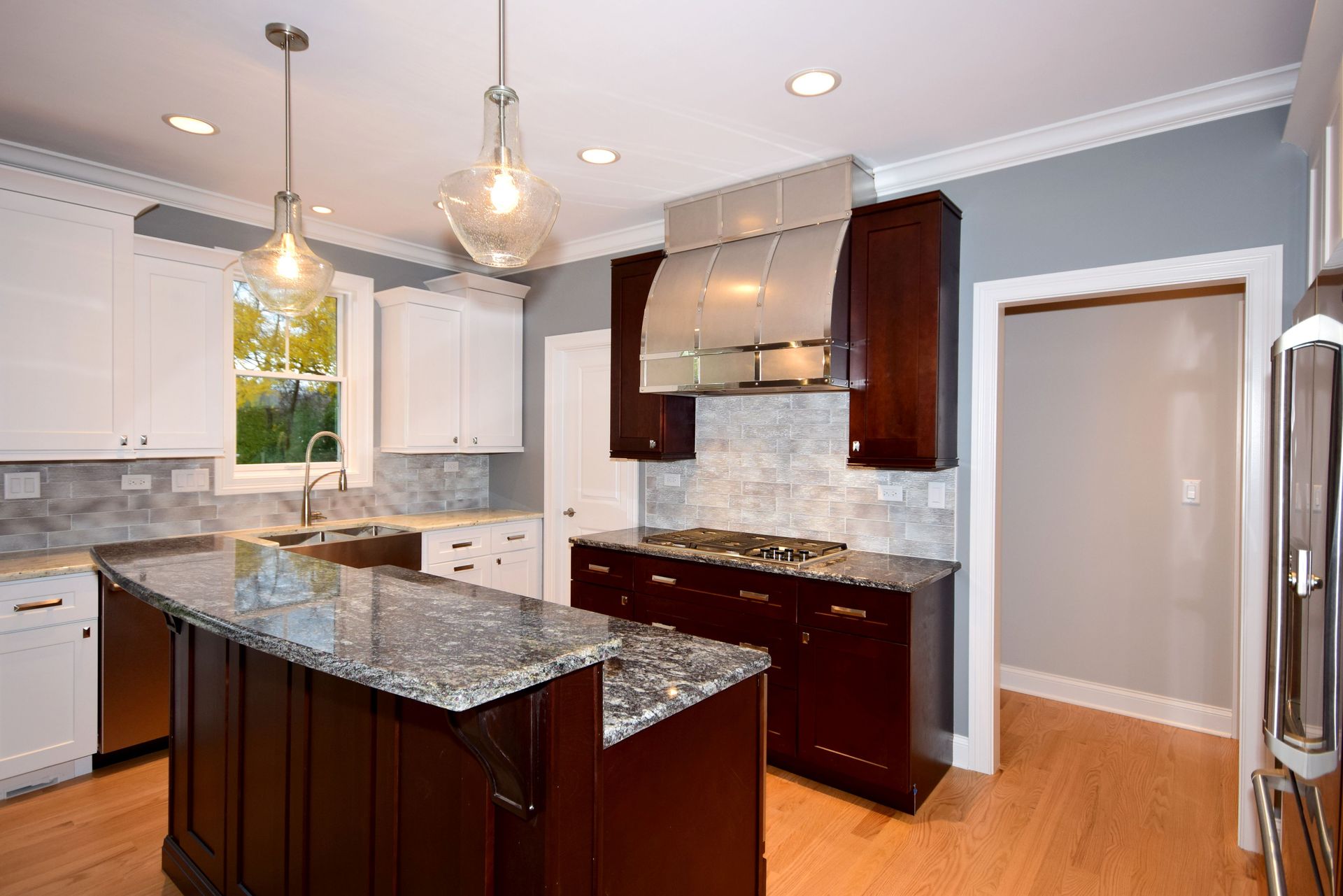 A kitchen with a large island , granite counter tops , stainless steel appliances and white cabinets.