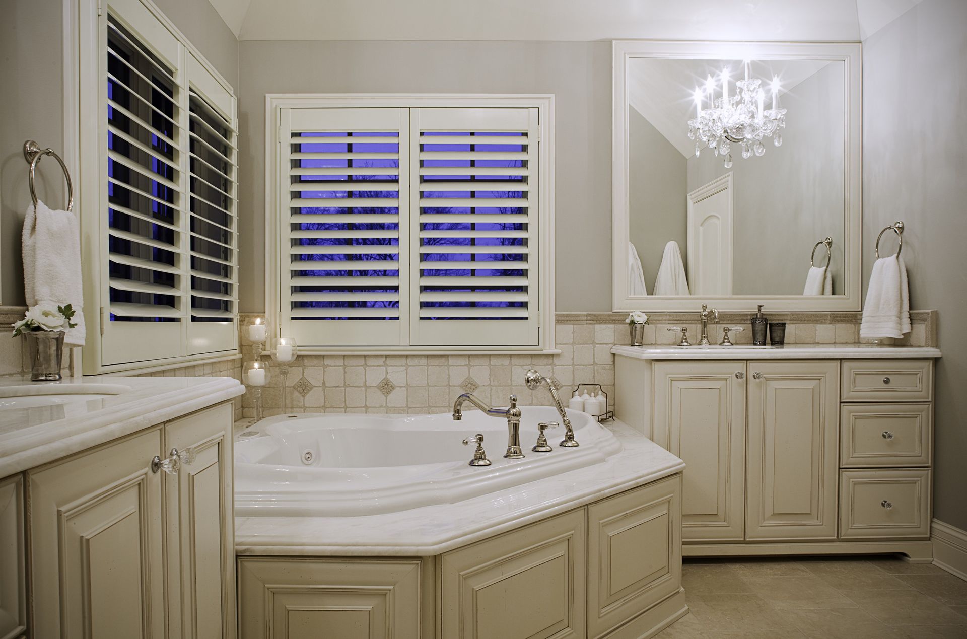 A bathroom with a tub , sink , mirror and shutters.