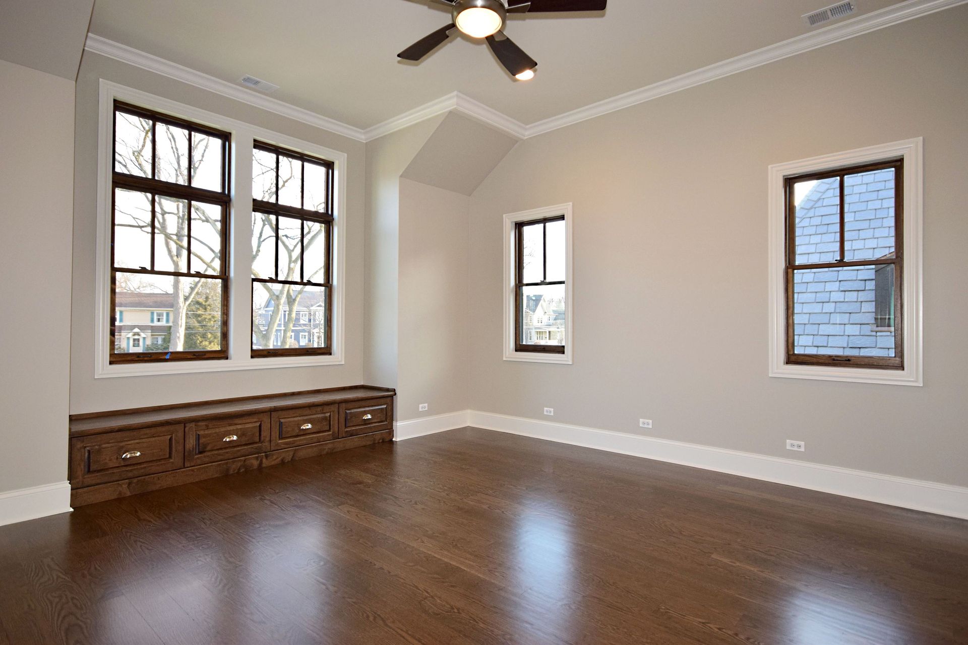An empty room with a ceiling fan and three windows.