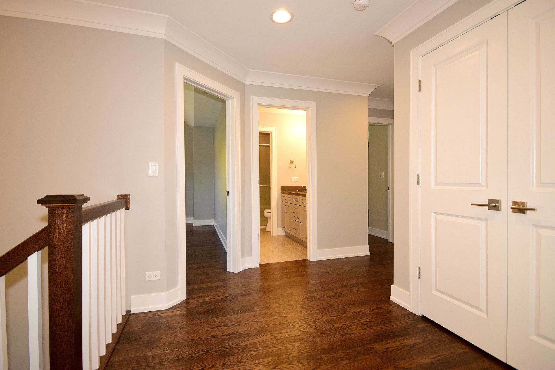 A hallway with a wooden railing leading to a bathroom.