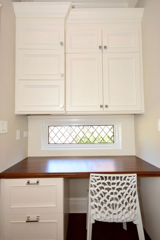 A desk with a chair underneath it and a window above it