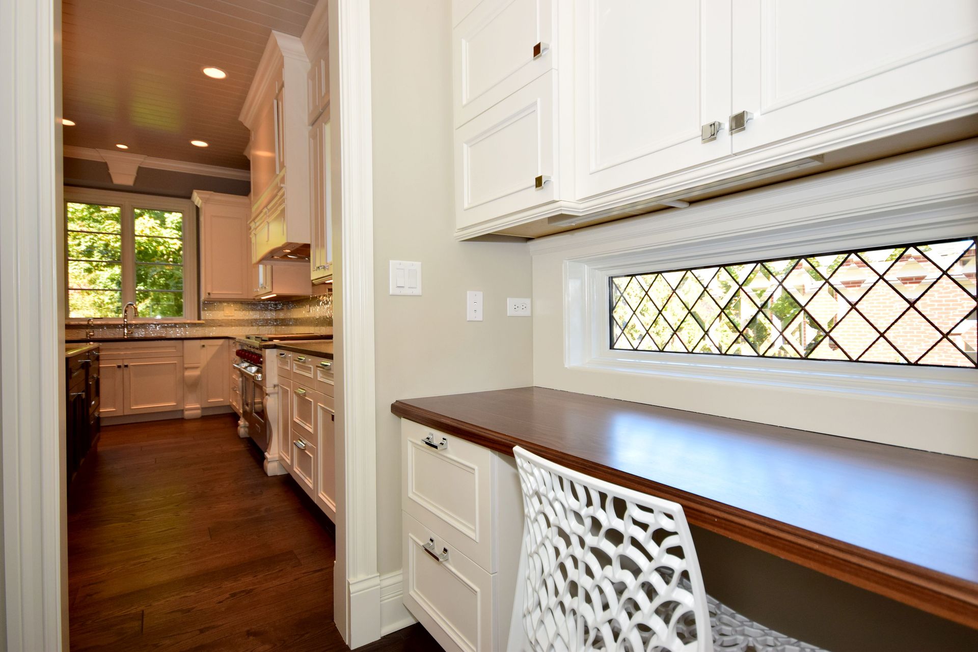 A kitchen with white cabinets and a desk with a stained glass window.