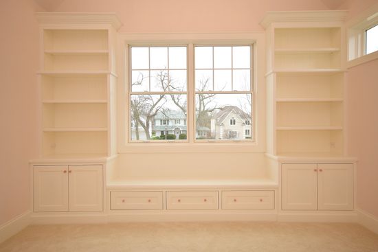 An empty room with shelves and a window with a view of a house