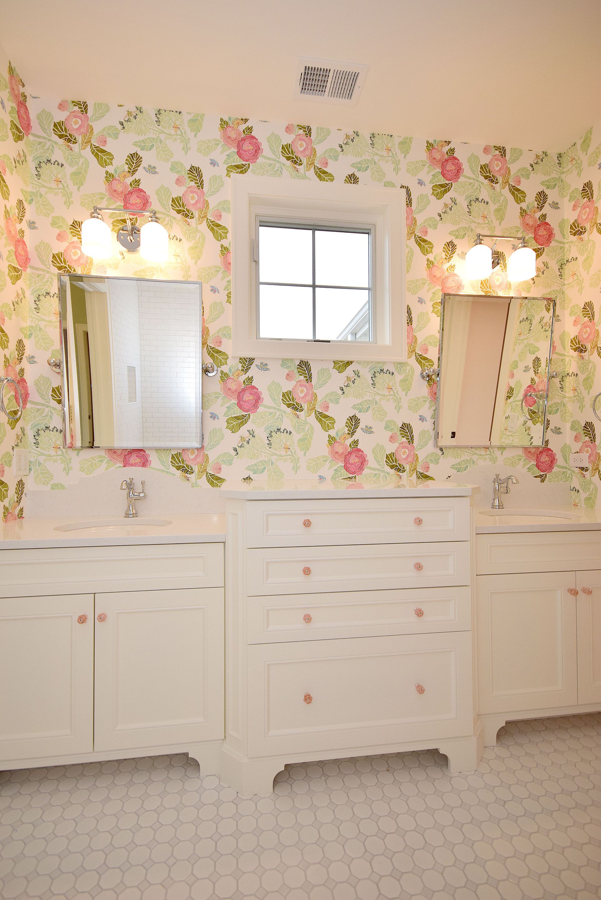 A bathroom with two sinks and two mirrors with floral wallpaper