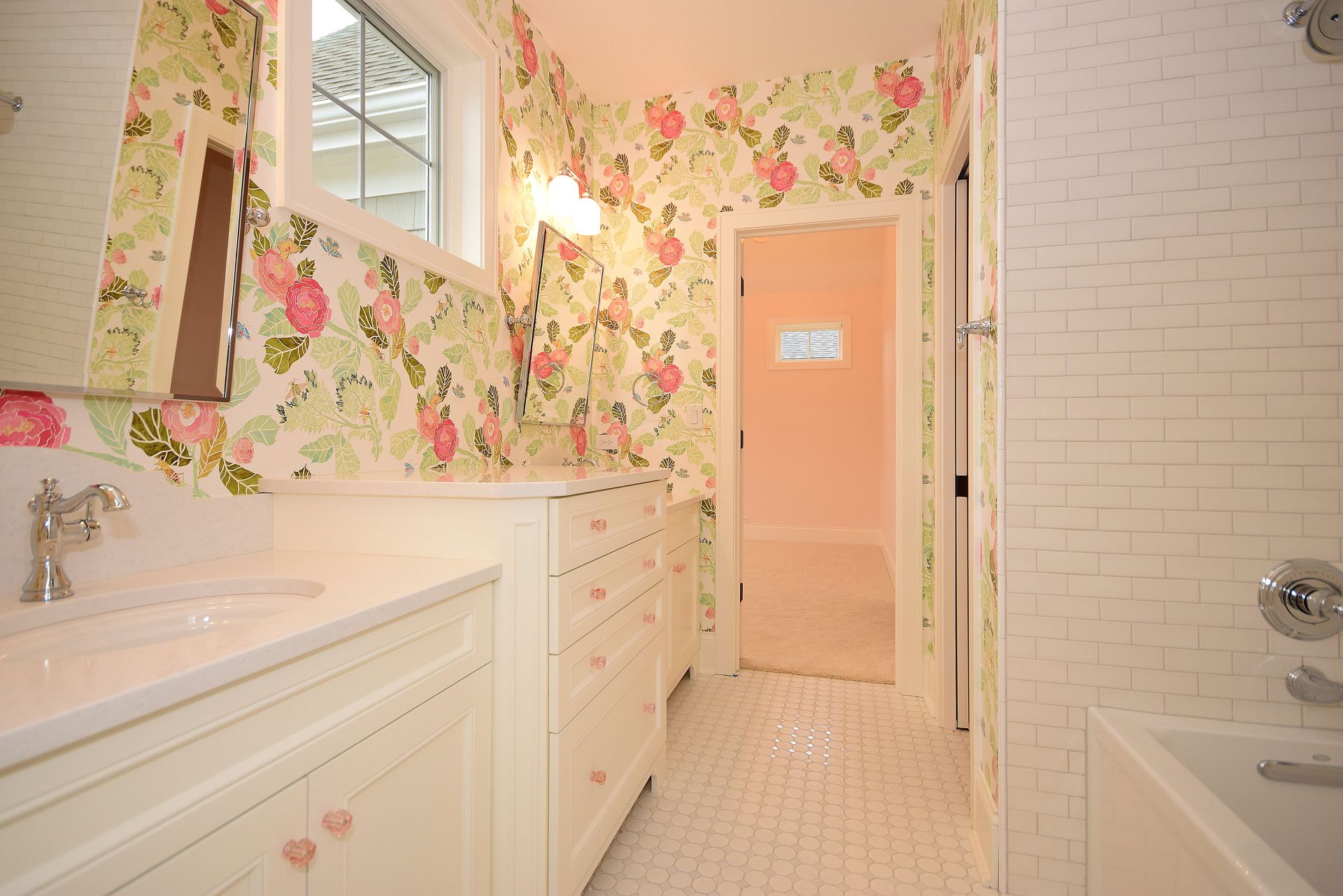 A bathroom with a sink , tub , mirror and floral wallpaper.