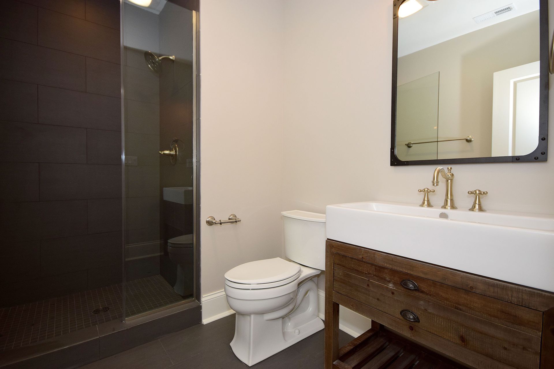 A bathroom with a toilet , sink , mirror and walk in shower.