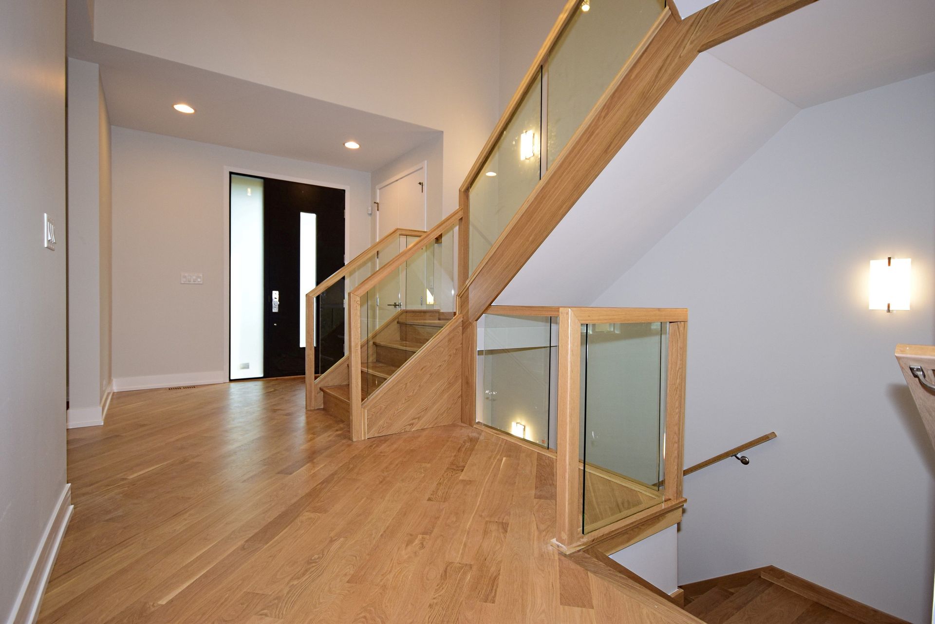 A hallway with a wooden staircase and a glass railing