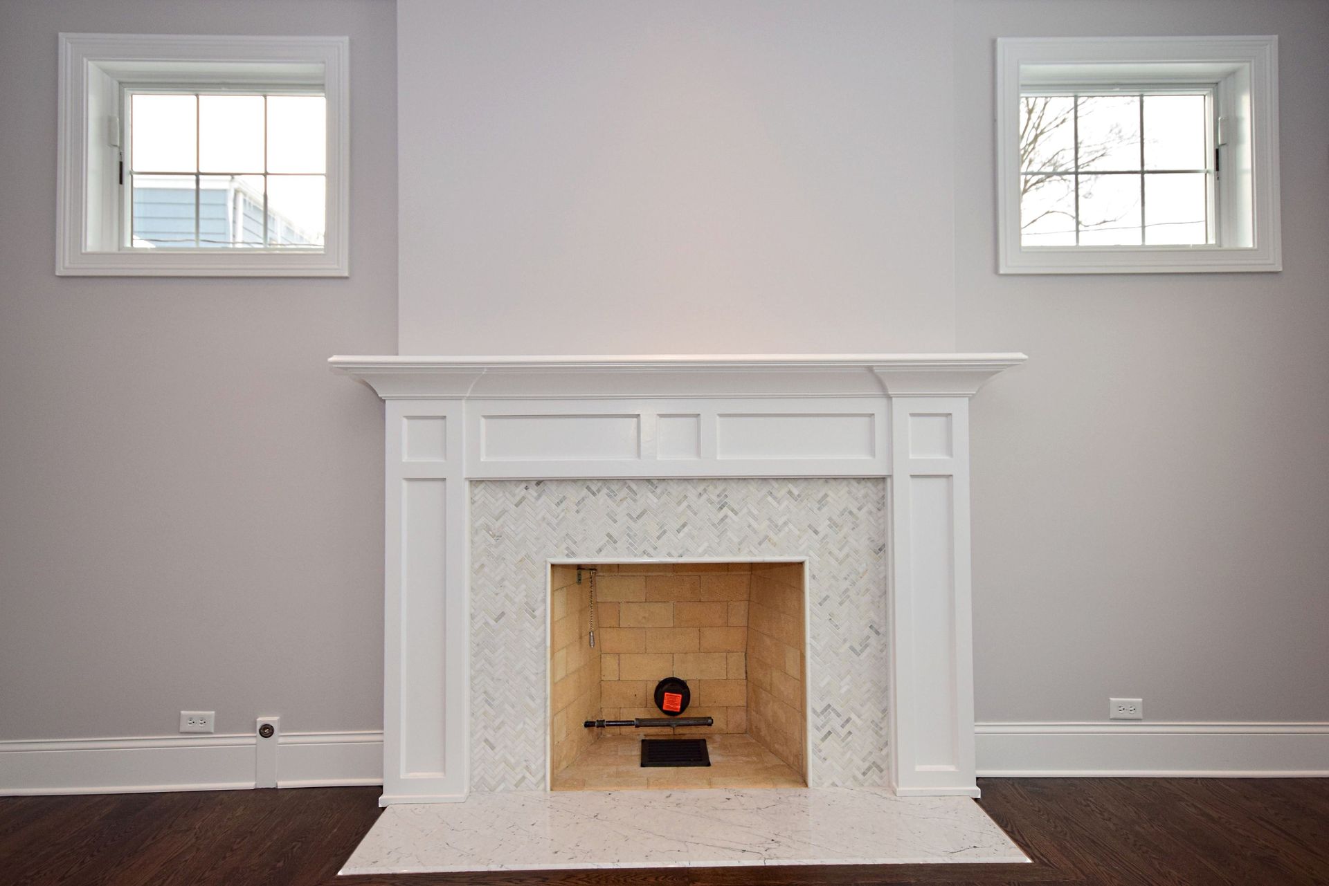An empty living room with a fireplace and two windows.
