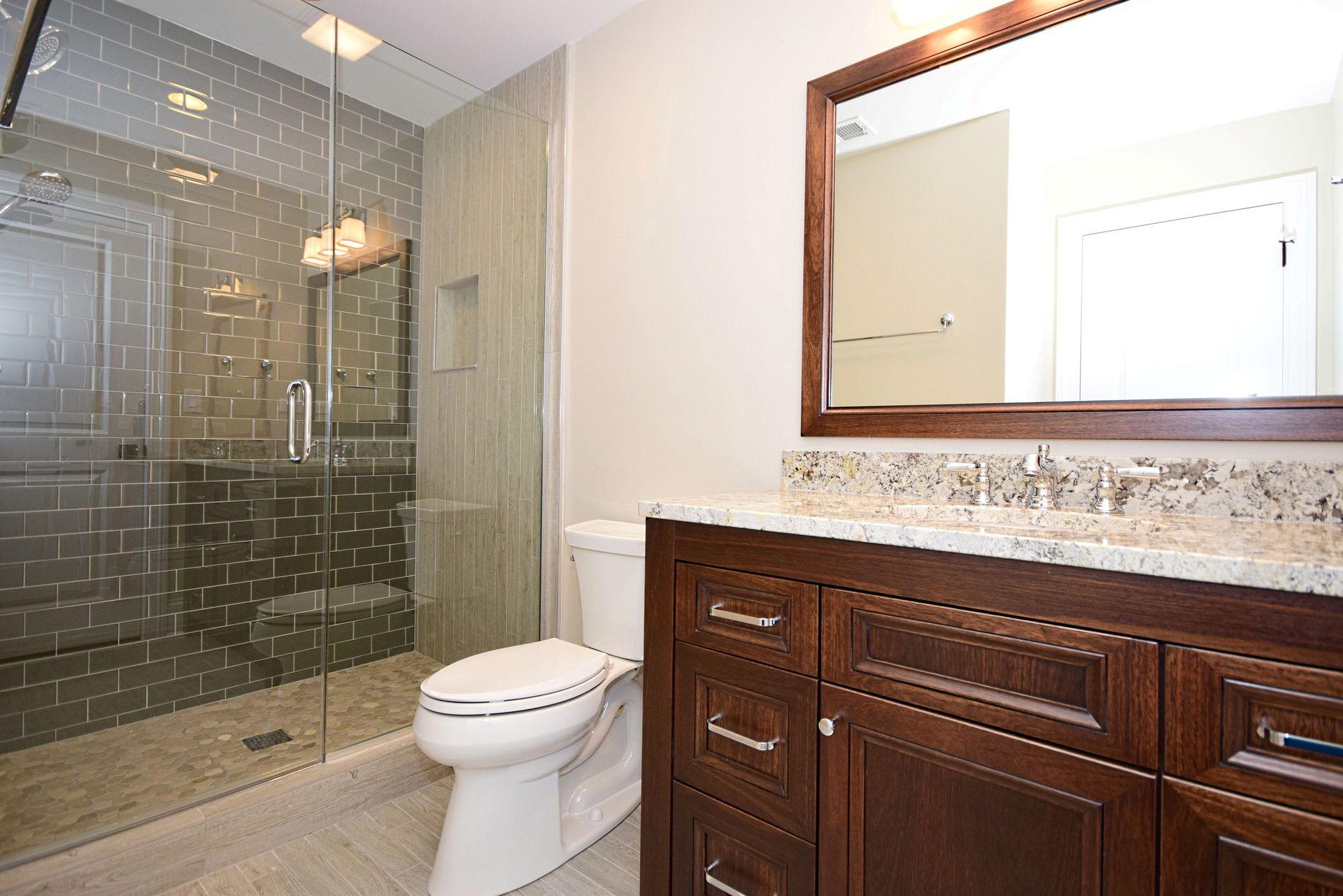 A bathroom with a toilet , sink , mirror and walk in shower.