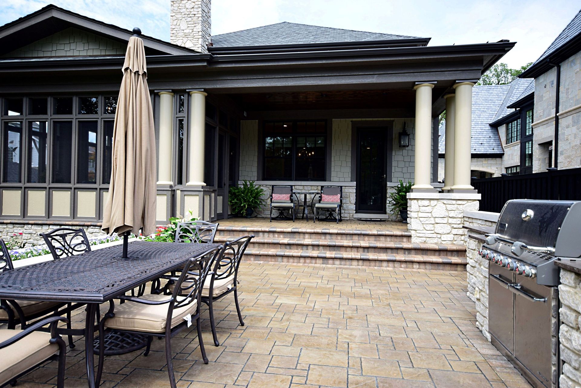 A patio with a table and chairs and a grill in front of a house.