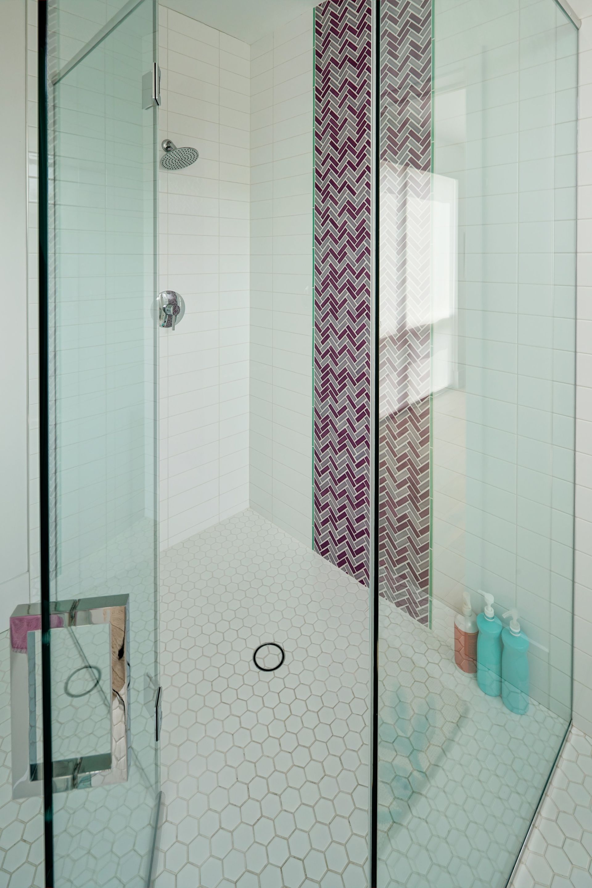 A bathroom with a walk in shower and a purple mosaic wall.