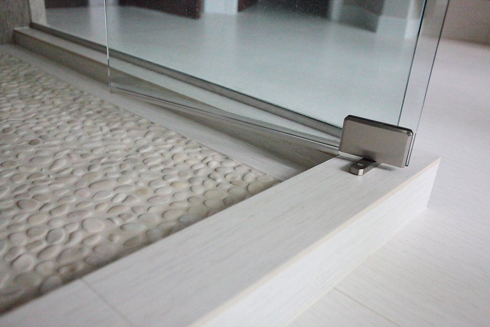A close up of a shower door with a stainless steel hinge.