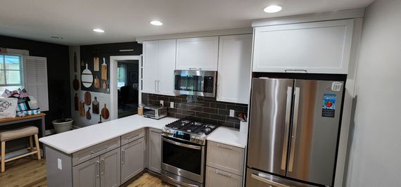 A modern kitchen featuring white cabinets, stainless steel appliances, a grey island, and a dark tile backsplash.