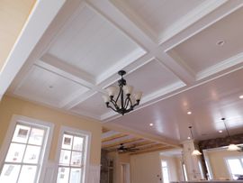 A coffered white ceiling with a chandelier in a room with light yellow walls and large windows.