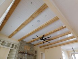 A ceiling with white shiplap panels between natural wood beams, recessed lighting, and a large black ceiling fan.