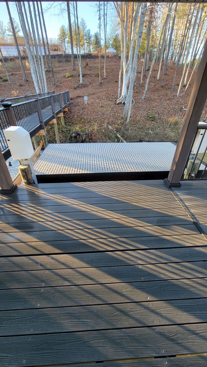A wooden deck with stairs leading up to a fenced in area with trees in the background.