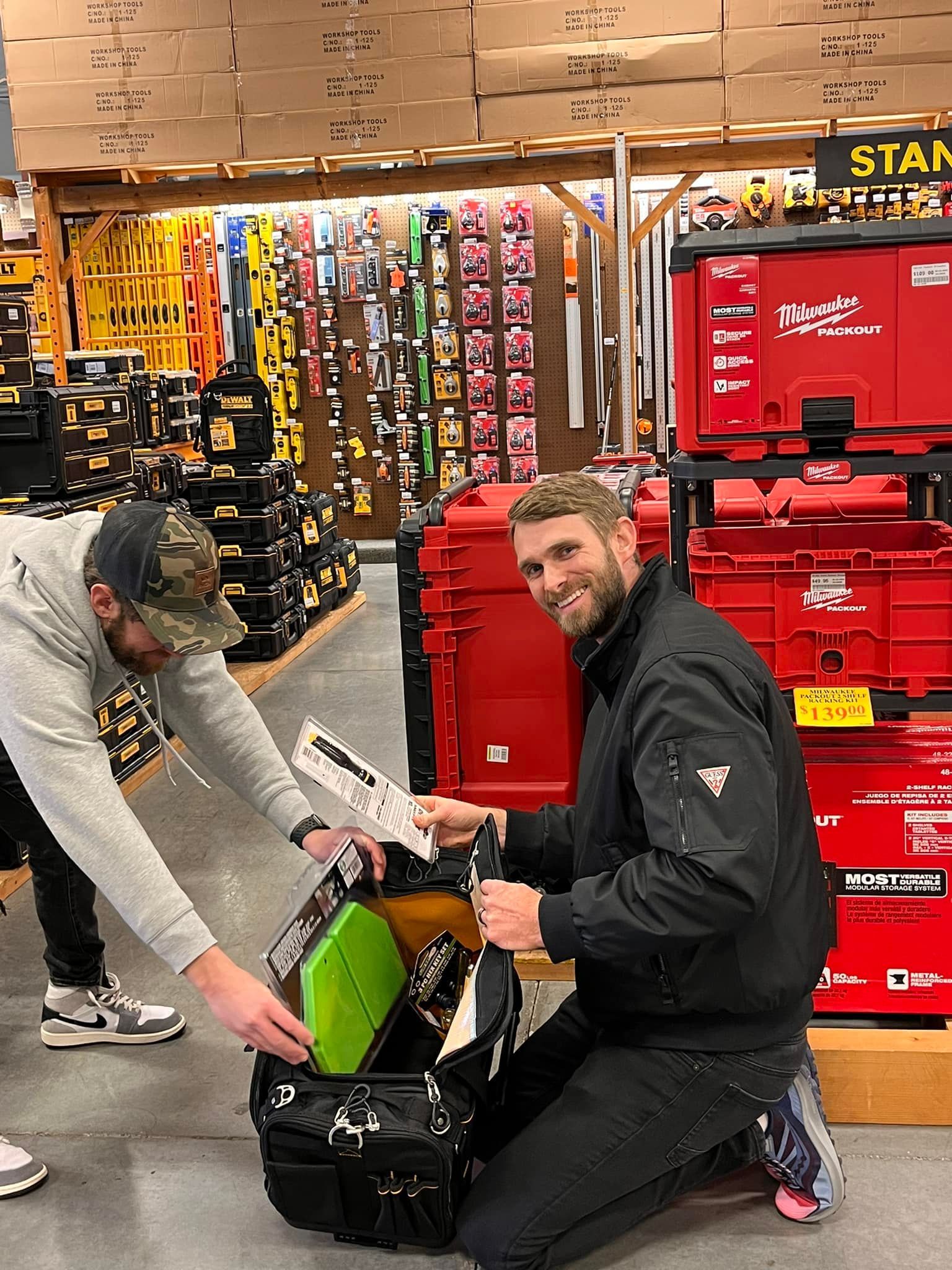 Two men are kneeling down in front of a toolbox in a store.