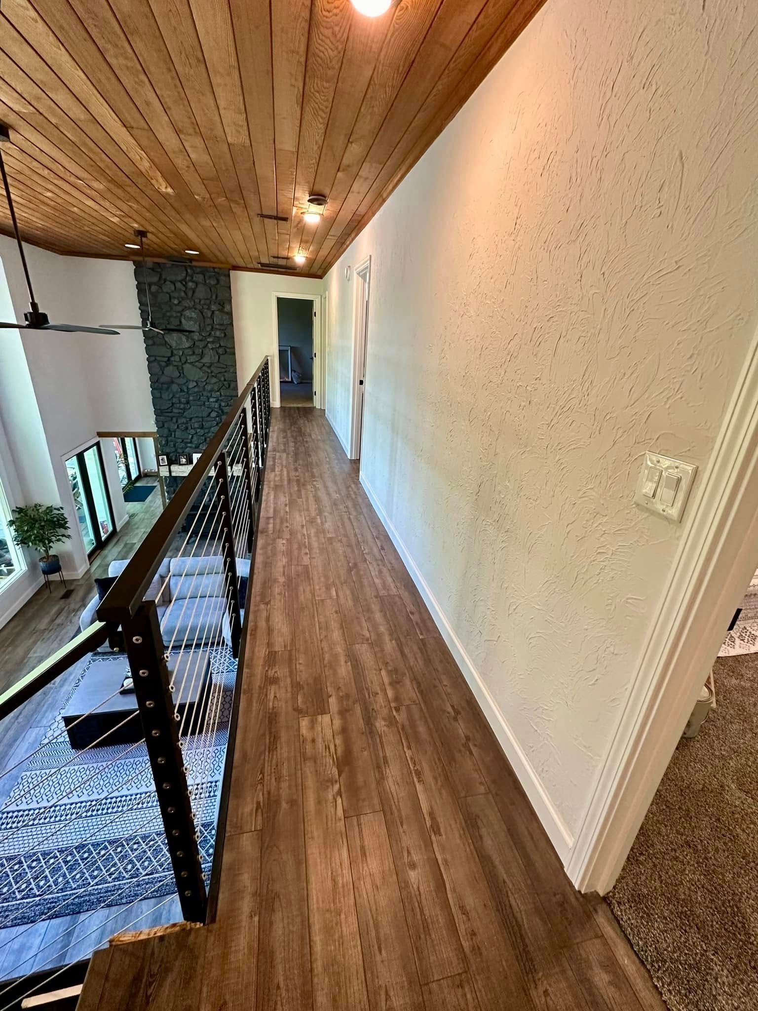 A long hallway with wooden floors and a railing in a house.