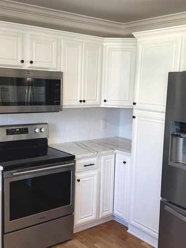 A kitchen with white cabinets , stainless steel appliances , a stove and a refrigerator.