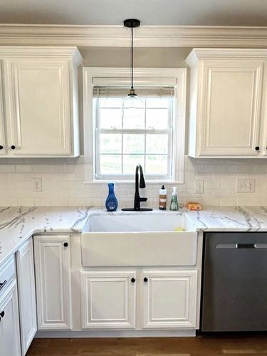 A kitchen with white cabinets , a farmhouse sink , a dishwasher , and a window.