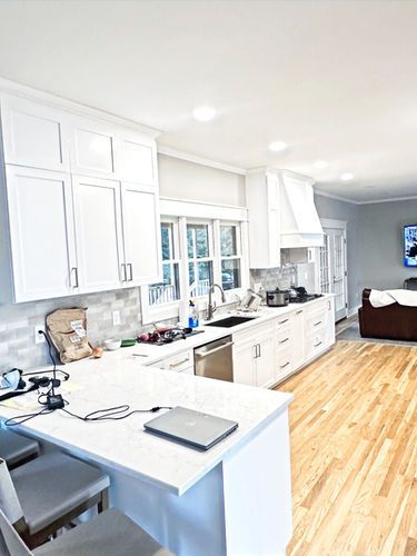 A kitchen with white cabinets and hardwood floors and a laptop on the counter.