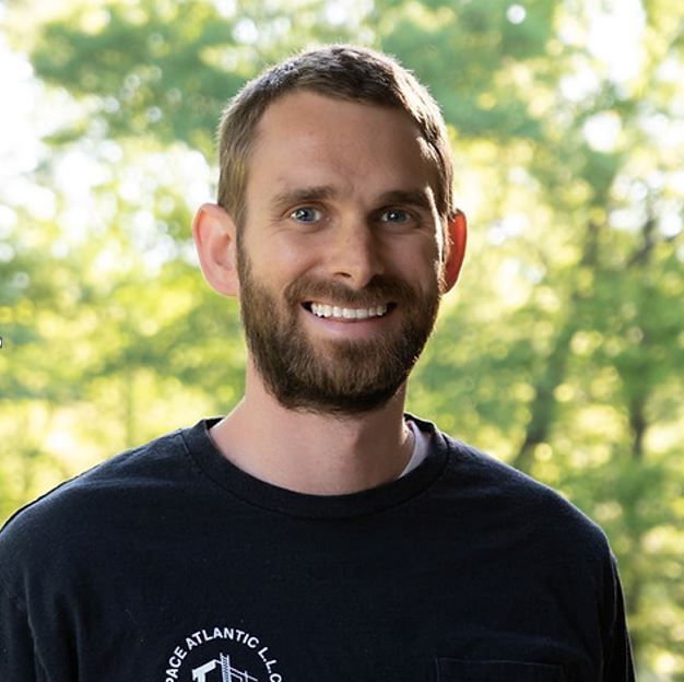 A man with a beard wearing a black t-shirt that says col atlantic llc
