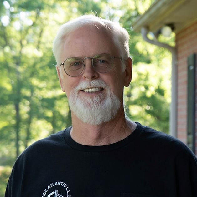A man with glasses and a beard is wearing a black shirt that says age atlantic lodge