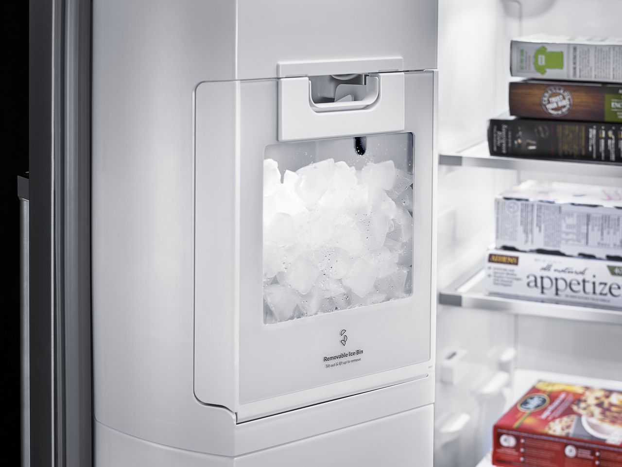 A white ice maker is sitting inside of a refrigerator.
