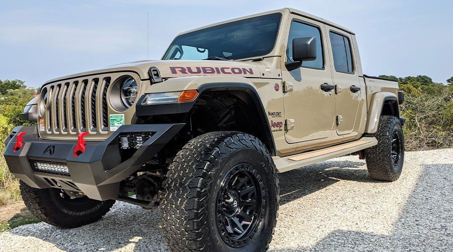 Tan Jeep Gladiator Rubicon with black accents parked on a gravel driveway.