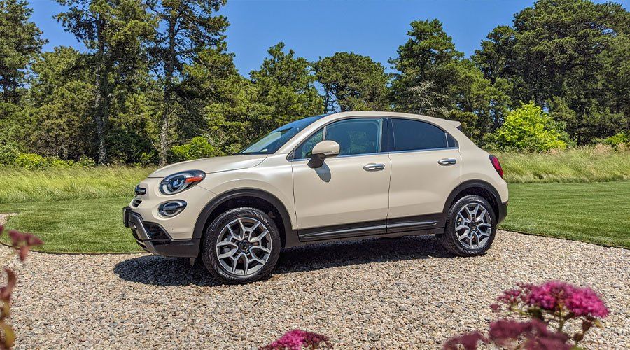A white car is parked on a gravel driveway in a field.