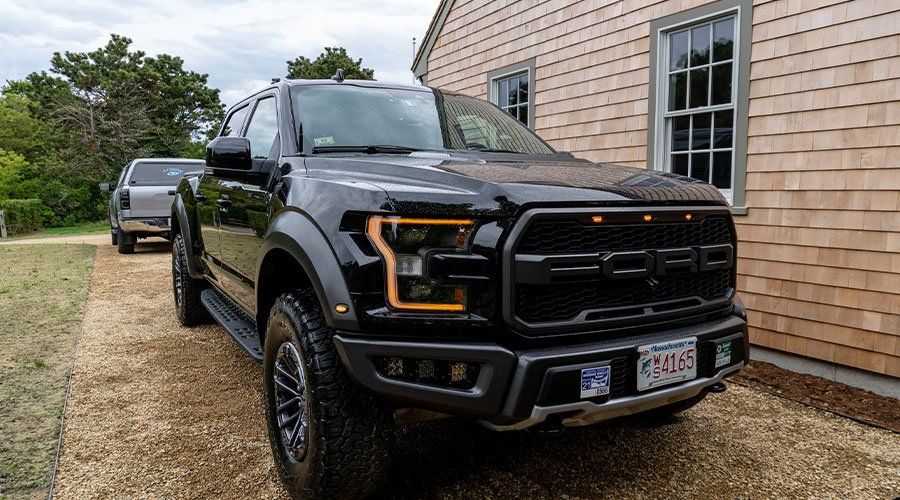 Black Ford Raptor pickup truck parked in front of a beige house.