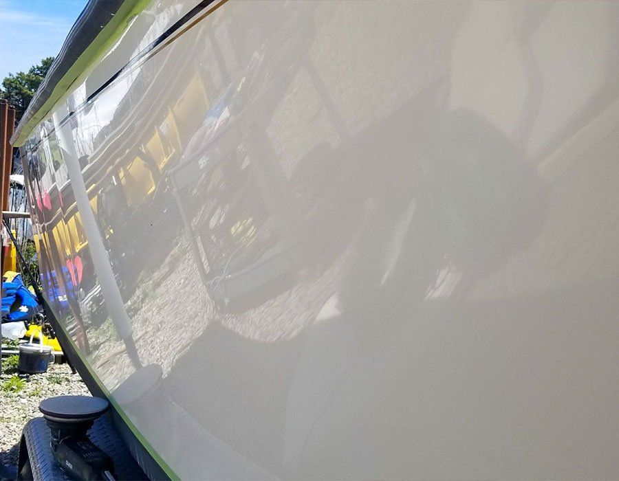 A shiny, white boat hull reflecting its surroundings, partially covered with green tape.