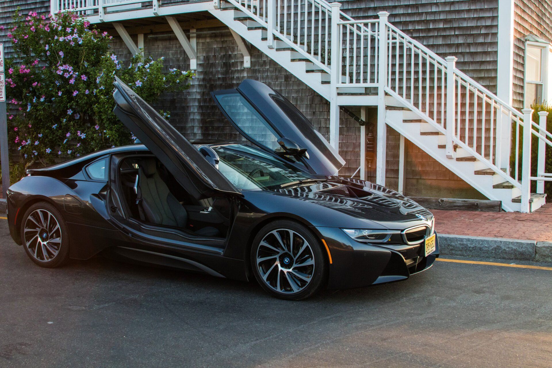 Black BMW i8 with open doors parked by stairs.