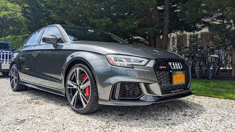 Gray Audi RS3 parked on gravel, with red brake calipers and black accents.