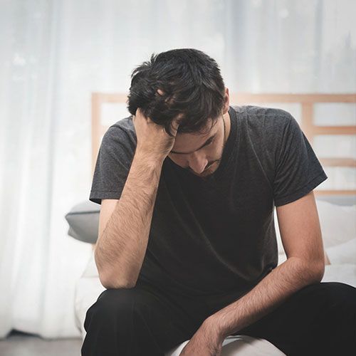 A man is sitting on a couch with his head in his hands.