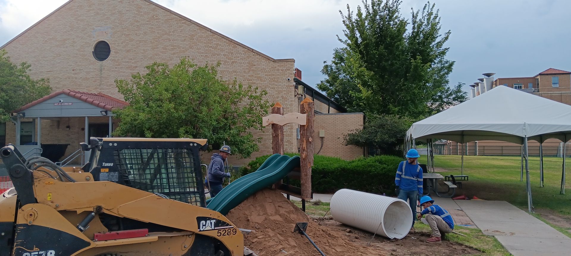 A large white pipe is sitting in the dirt in front of a building.