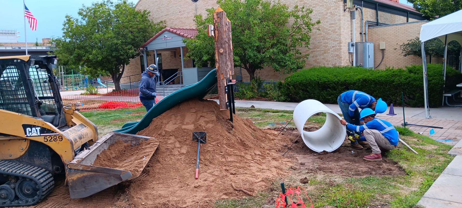 A group of construction workers are working on a large pile of dirt in front of a building.