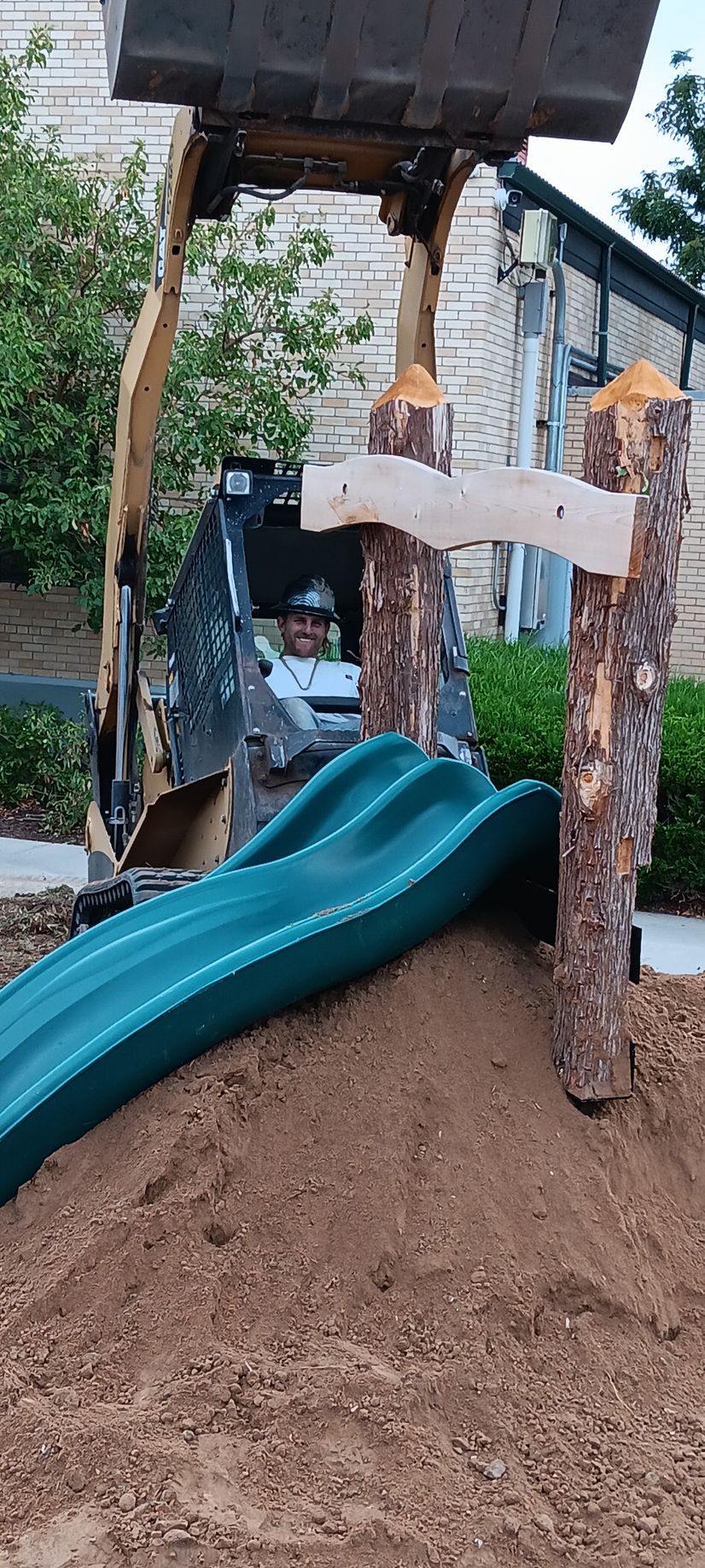 A bulldozer is loading dirt into a playground with a slide.